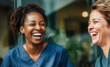 Eine weiße und eine farbige Krankenschwester lachen zusammen 